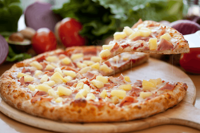 An image of pizza with ham and pineapple on it.