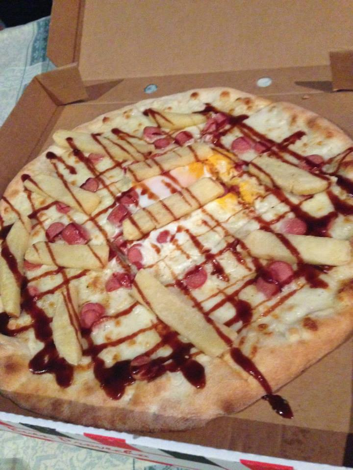 A pizza topped with hot dog slices, steak fries, with barbecue sauce drizzled on top.